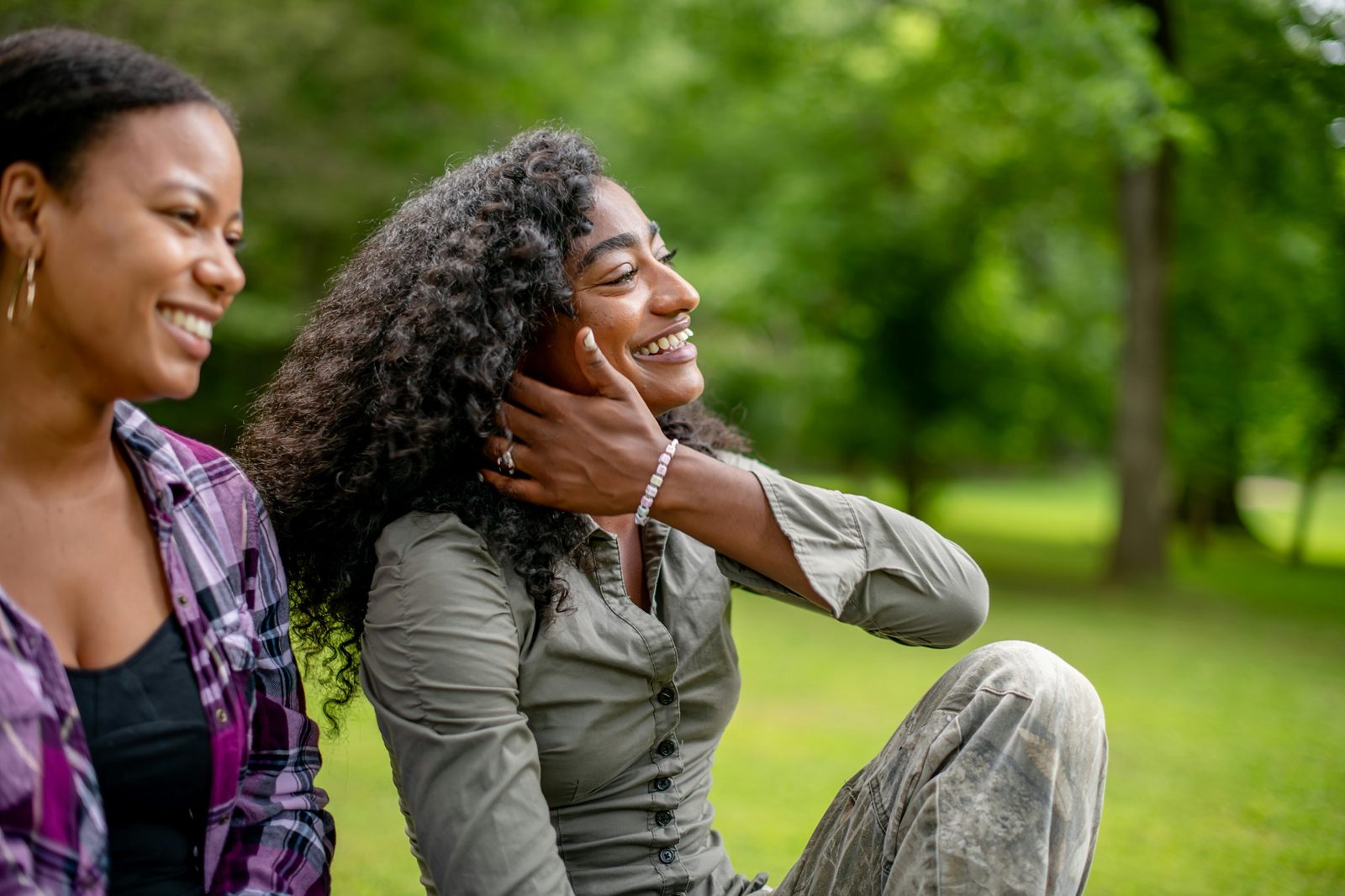 Two young women laughing together on the grass in a sunny park